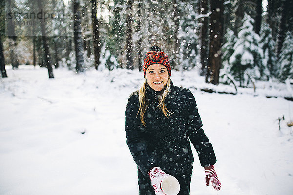 Frau in schneebedecktem Wald wirft Schnee aus Tasse