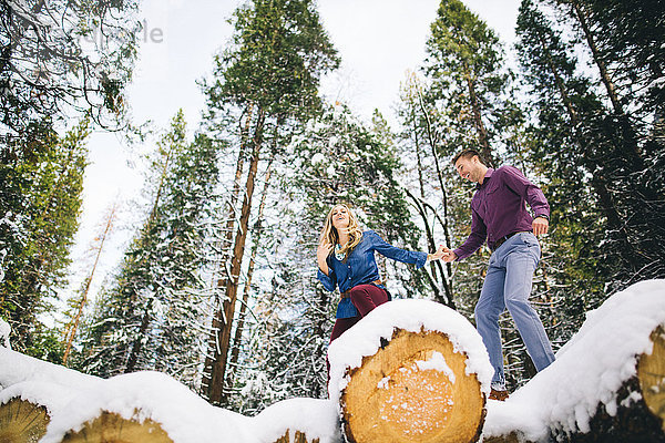 Paar im Wald klettert auf schneebedeckte Baumstämme