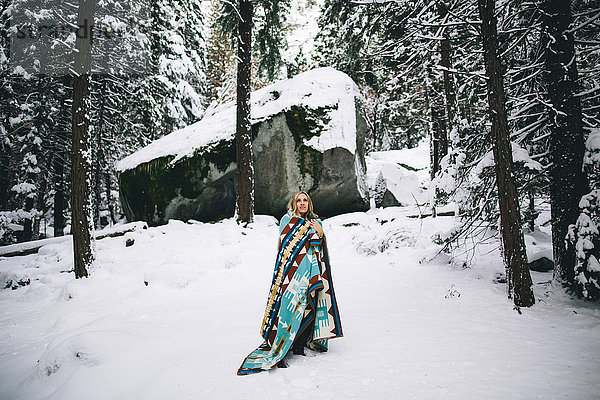 Frau in schneebedecktem Wald in Decke gehüllt