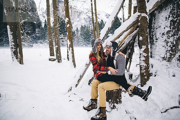 Frau sitzt auf dem Schoss eines Mannes in schneebedeckter Landschaft