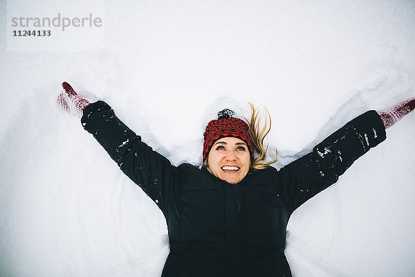 Frau auf dem Rücken liegend mit offenen Armen im Schnee