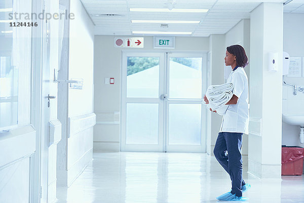 Weibliche Pflegerin trägt Handtücher auf dem Krankenhauskorridor