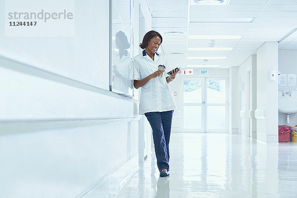 Weibliche Pflegerin liest auf dem Krankenhauskorridor Smartphone-Texte