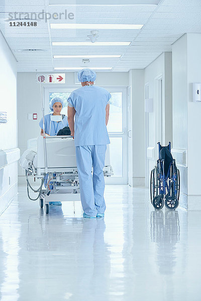 Männliche und weibliche Krankenschwestern schieben das Bett auf dem Krankenhauskorridor