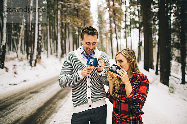 Ehepaar im schneebedeckten Wald trinkt Heißgetränk aus Bechern