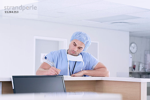 Männlicher Arzt schreibt medizinische Notizen auf der Krankenschwesterstation im Krankenhaus