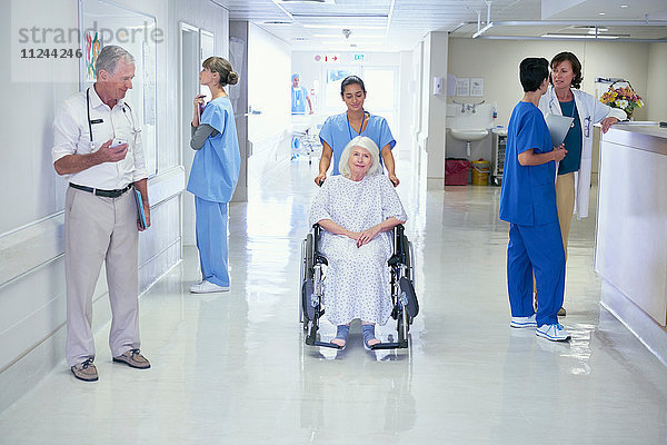 Krankenschwester schiebt ältere Patientin im Rollstuhl auf die Krankenhausstation