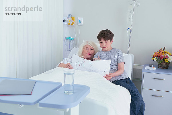 Ältere Patientin im Krankenhausbett mit Blick auf die Zeichnung ihres Enkels
