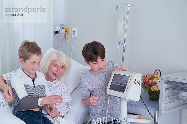 Ältere Patientin im Krankenhausbett mit Enkeln  die mit einem Blutdruckmessgerät spielen