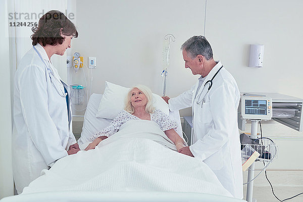 Zwei Ärzte im Gespräch mit einer älteren Patientin im Krankenhausbett