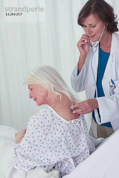 Ärztin  die einer älteren Patientin mit dem Stethoskop zuhört