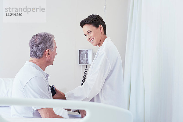 Ärztin benutzt Blutdruckmesser bei älterem männlichen Patienten am Krankenhausbett