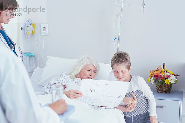 Ältere Patientin im Krankenhausbett mit Blick auf die Zeichnung ihres Enkels