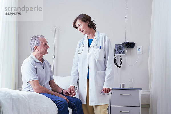 Ärztinnen erklären einem älteren männlichen Patienten im Krankenhausbett