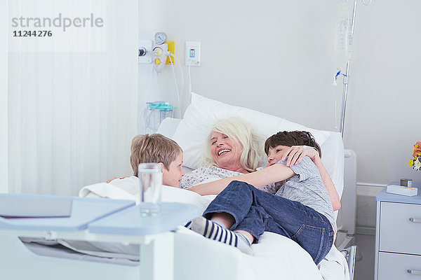 Ältere Patientin kuschelt Enkel auf Krankenhausbett
