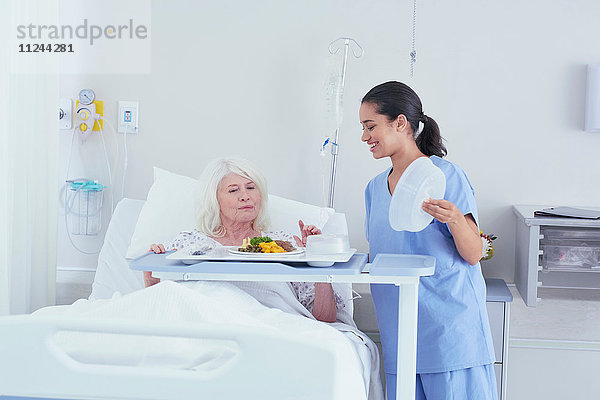 Krankenschwester serviert Mittagessen für ältere Patientin im Krankenhausbett