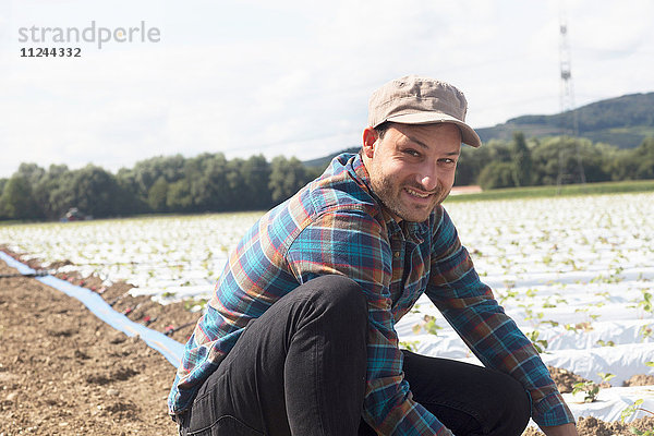 Landwirt auf dem Feld  der sich um Setzlinge kümmert und lächelnd in die Kamera schaut