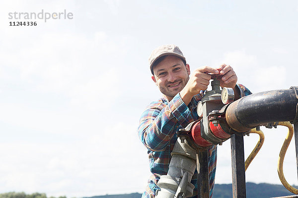Mann öffnet Ventil an Industrierohrleitungen und schaut lächelnd in die Kamera