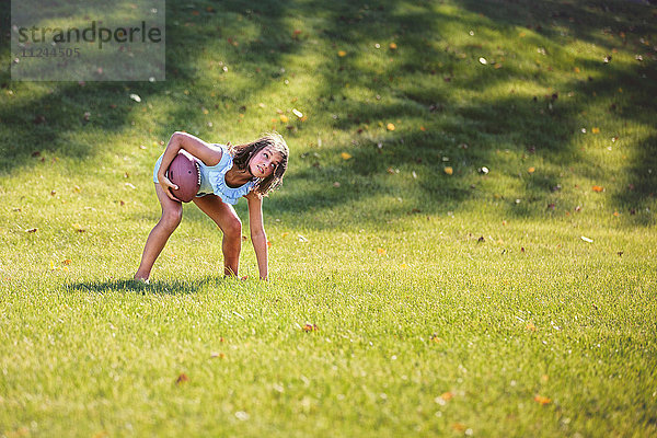 Mädchen beugt sich vor und spielt American Football im Park