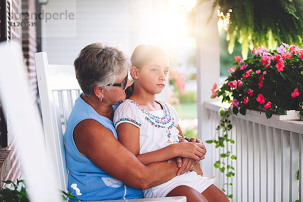 Mädchen sitzt auf Großmutters Schoß in der Veranda bei Sonnenuntergang