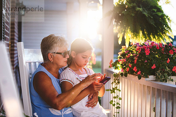 Mädchen und Großmutter spielen Smartphone-Spiel auf der Veranda bei Sonnenuntergang