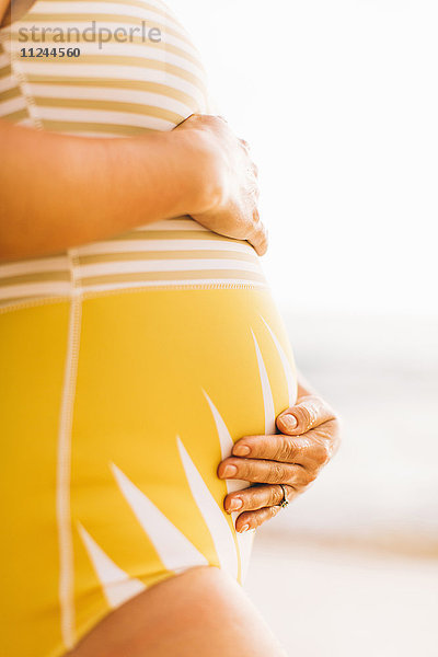 Mittlerer Abschnitt einer schwangeren  mittleren erwachsenen Frau mit Bauchhaltung Makua Beach  Hawaii  USA