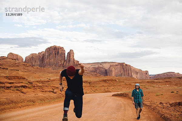 Zwei Männer  ein sprintender und ein gehender auf Feldweg  Monument Valley  Arizona  USA