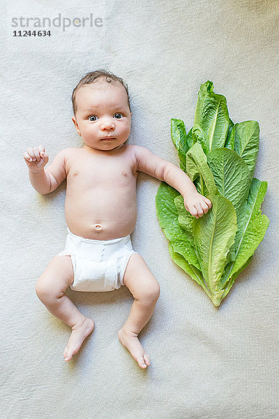 Neugeborener Junge liegt neben Salatblättern
