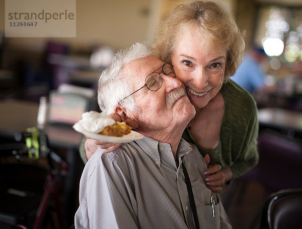 Ältere Frau umarmt älteren Mann und lächelt