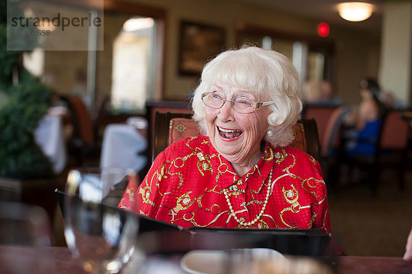 Ältere Frau sitzt am Tisch im Restaurant und lacht