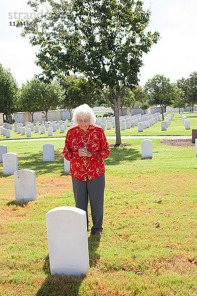 Ältere Frau steht neben Grabstein auf dem Friedhof