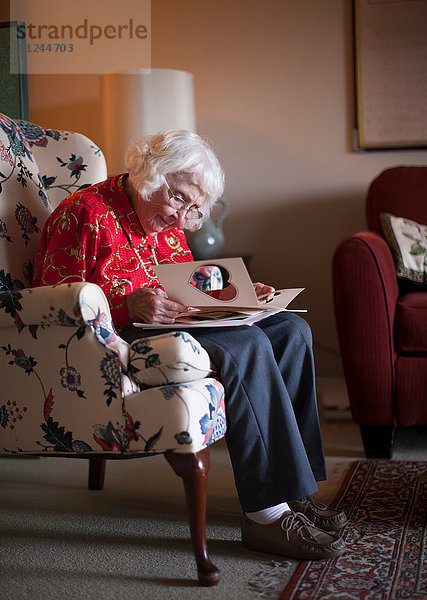 Ältere Frau sitzt auf einem Stuhl und schaut auf eine Grußkarte