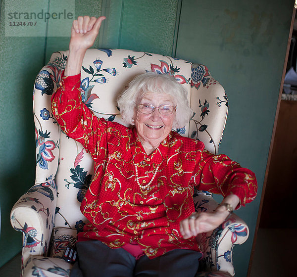 Porträt einer älteren Frau auf einem Stuhl sitzend  lächelnd  den Arm erhoben