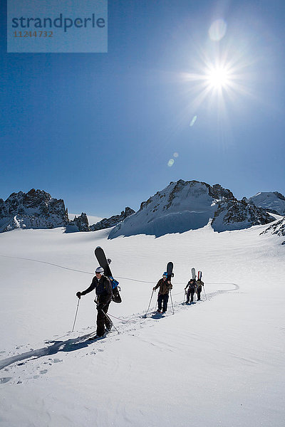 Vier männliche Snowboarder wandern durch verschneite Landschaft  Trient  Schweizer Alpen  Schweiz