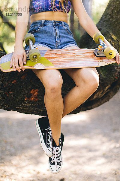 Frau mit Skateboard auf Baum sitzend