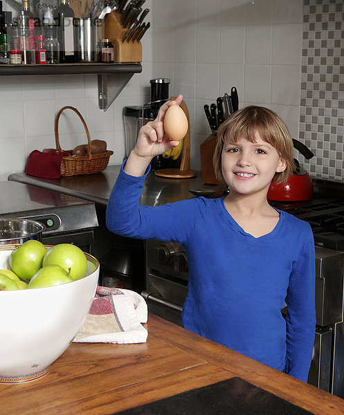 Porträt eines jungen Mädchens  das in der Küche steht und ein Ei hält