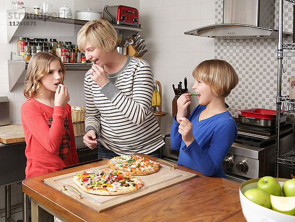 Mutter und zwei Töchter in der Küche bei der Essenszubereitung  knabbern an Zutaten