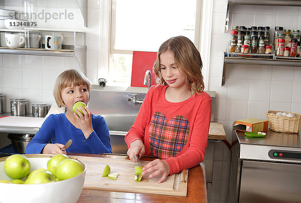 Zwei junge Mädchen in der Küche  die auf einem Schneidebrett Äpfel schneiden