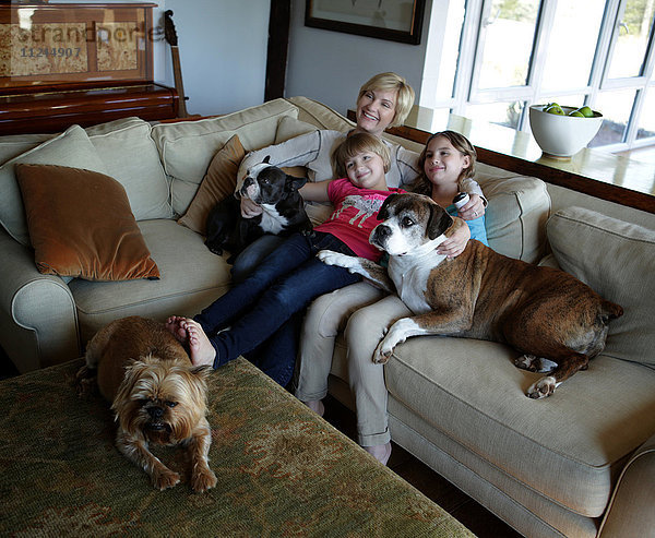 Mutter und Töchter sitzen mit ihren Hunden auf dem Sofa und sehen gemeinsam fern