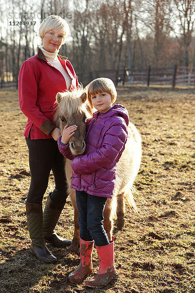Porträt von Mutter und Tochter im Freien  stehend mit Pony