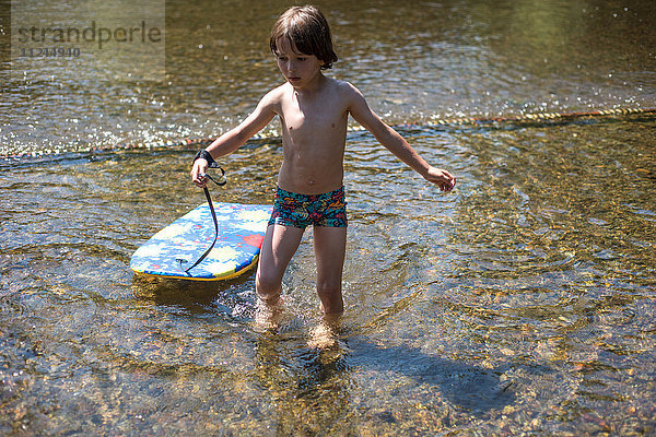 Junge knöcheltief im Wasser mit Körperbrett