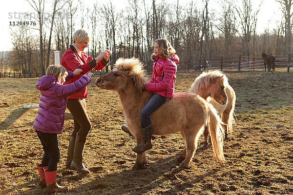 Junges Mädchen auf Pony reitend  Mutter und Schwester neben ihnen stehend