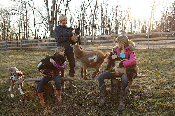Mutter und Töchter im Freien  Ziegen und Haushund umarmend