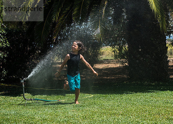 Junge  der durch Wasser aus einem Gartensprinkler läuft