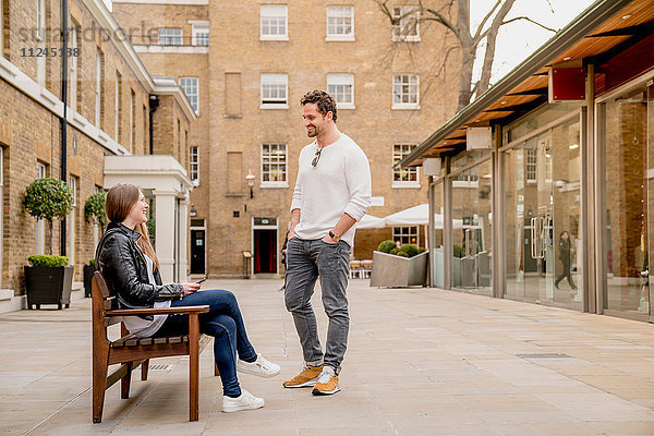 Junger Mann begrüsst Freundin auf Bank sitzend  Kings Road  London  UK