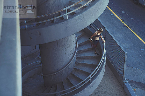 Junge Frau streckt sich auf einer Wendeltreppe im Freien