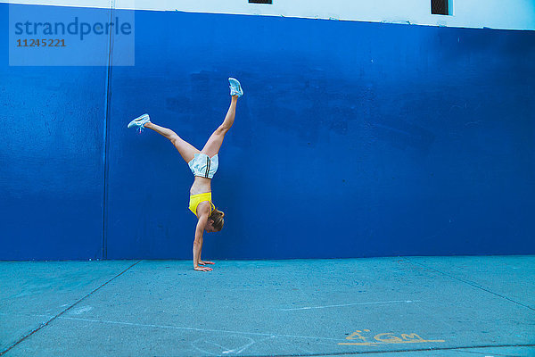 Junge Frau macht Handstand im Freien vor blauer Wand