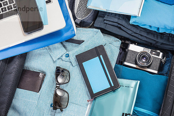 Detail eines gepackten Koffers mit blauem Hemd  Retro-Kamera  Laptop  Smartphone und Notizbuch