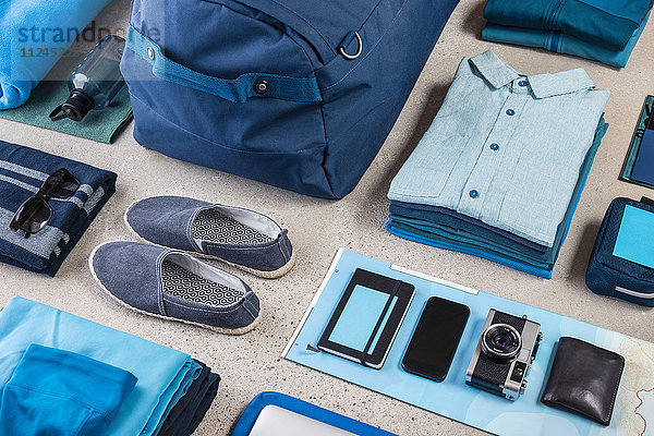 Draufsicht auf die Reisepackung mit blauem Hemd  Retro-Kamera  Trainingsschuhen  Smartphone und Notebook
