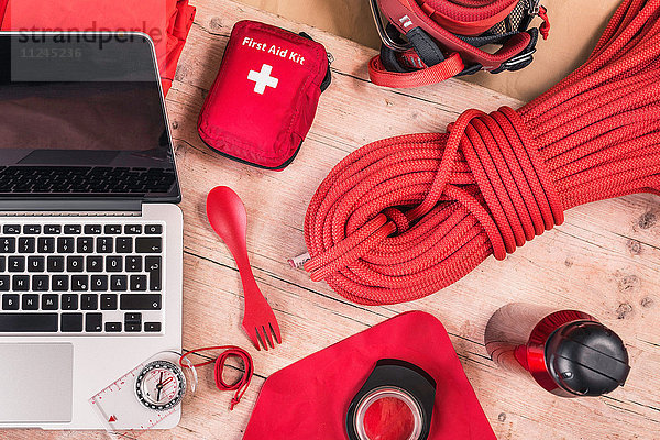 Draufsicht auf das Packen der Kletterausrüstung mit rotem Erste-Hilfe-Kasten  Kletterseilen und Laptop